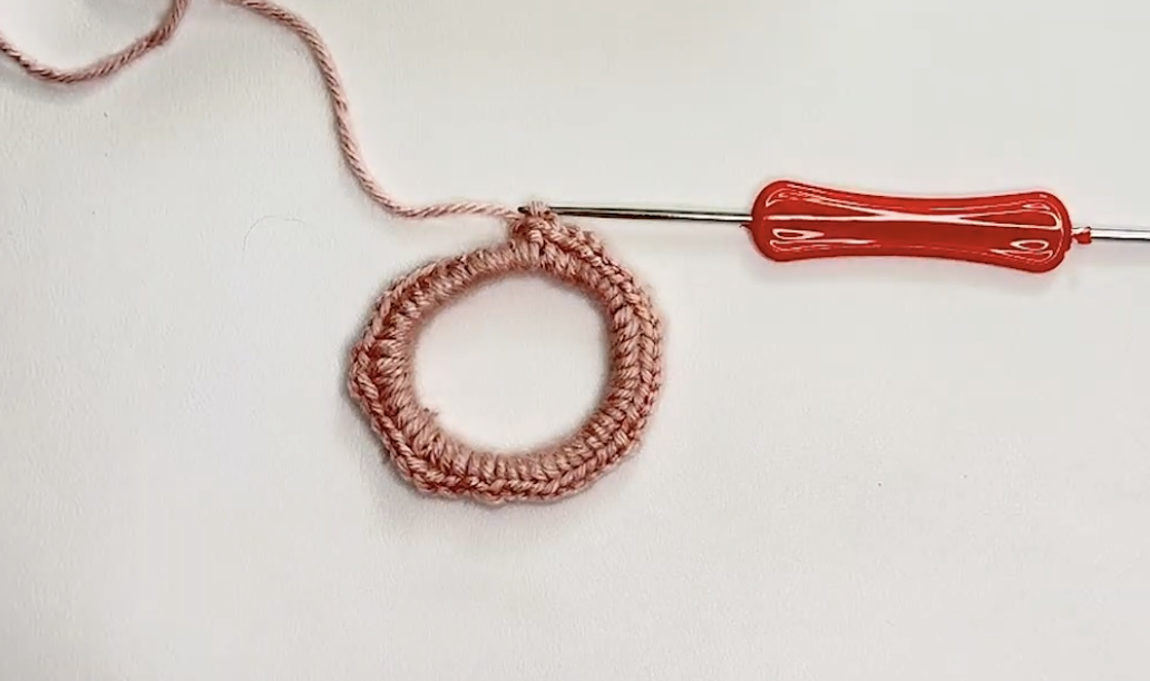 Hair tie covered with pink single crochet stitches after round 1