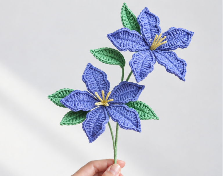 Two purple crochet hibiscus flowers with yellow centers and green leaves on a wrapped stem