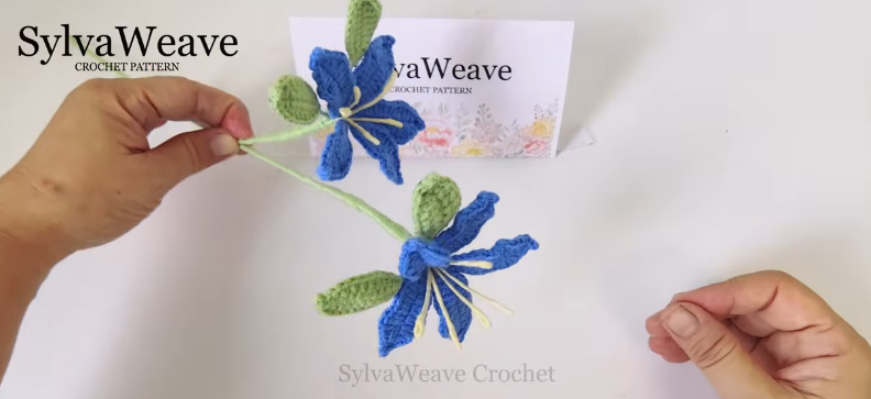 Two assembled crochet hibiscus flowers attached to a green yarn-wrapped stem