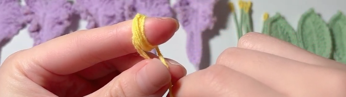 Wrapping yellow yarn around a finger to make the flower centre